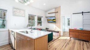 A modern kitchen with a central island, wooden cabinets, and a large window. - Charming Treehouse Escape Among Nature's Blooms (Pittsboro)