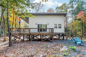 A cabin with a deck, surrounded by trees and a gravel ground. - Charming Treehouse Escape Among Nature's Blooms (Pittsboro)