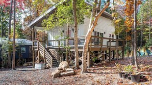 A cabin with a wooden deck, a staircase, and a view of the surrounding forest. - Charming Treehouse Escape Among Nature's Blooms (Pittsboro)