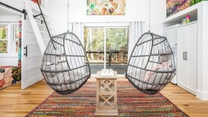 A room with two hanging egg chairs, a colorful rug, a white cabinet, and a painting on the wall. - Charming Treehouse Escape Among Nature's Blooms (Pittsboro)
