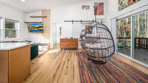 A modern interior with a kitchen island, a hanging chair, and a large window. - Charming Treehouse Escape Among Nature's Blooms (Pittsboro)