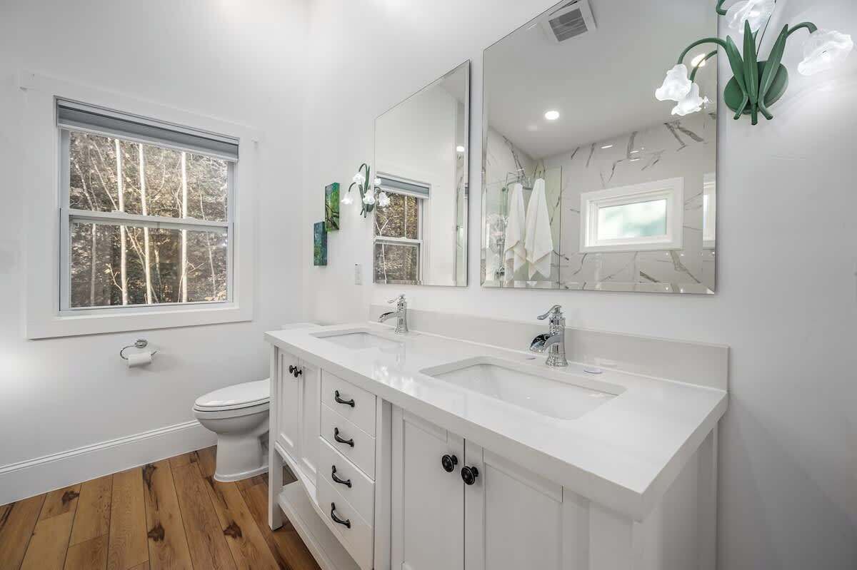 A modern bathroom with a double sink vanity, a large mirror, and a toilet.