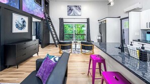 A modern living space with a sofa, two chairs, a dining table, a kitchen area, and artwork on the walls. - Two Unique Treehouses in Nature (Pittsboro)