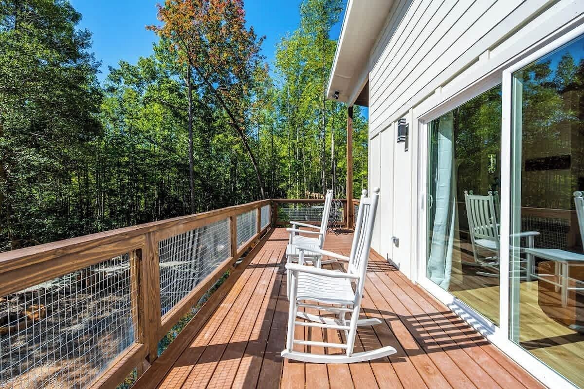 Une terrasse en bois avec des fauteuils à bascule blancs et une porte vitrée donnant sur un espace abrité.