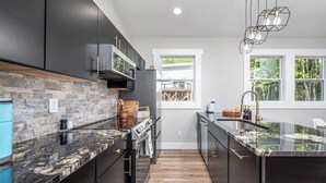Een moderne keuken met donkere kastjes, een stenen spatwand en een centraal eiland.