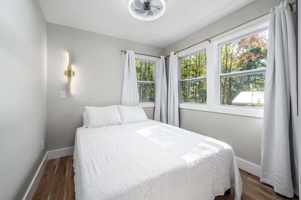 Une chambre à coucher avec un lit, un ventilateur de plafond et de grandes fenêtres avec des rideaux.
