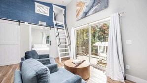 Een moderne woonkamer met een blauwe bank, een houten salontafel, een witte trap en een schuifpui naar een balkon.
