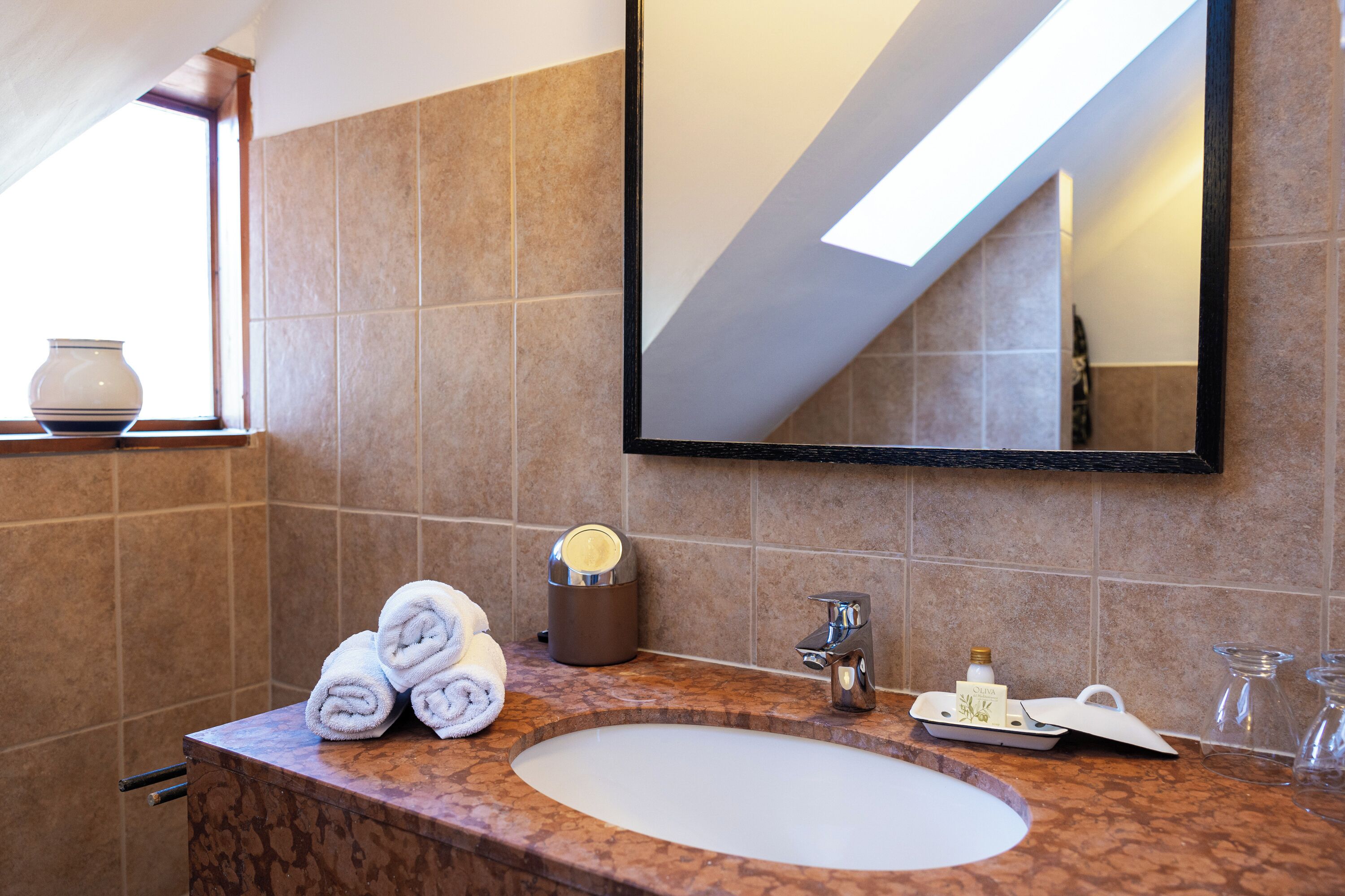 A bathroom with a marble sink, a large mirror, and a window with a vase.