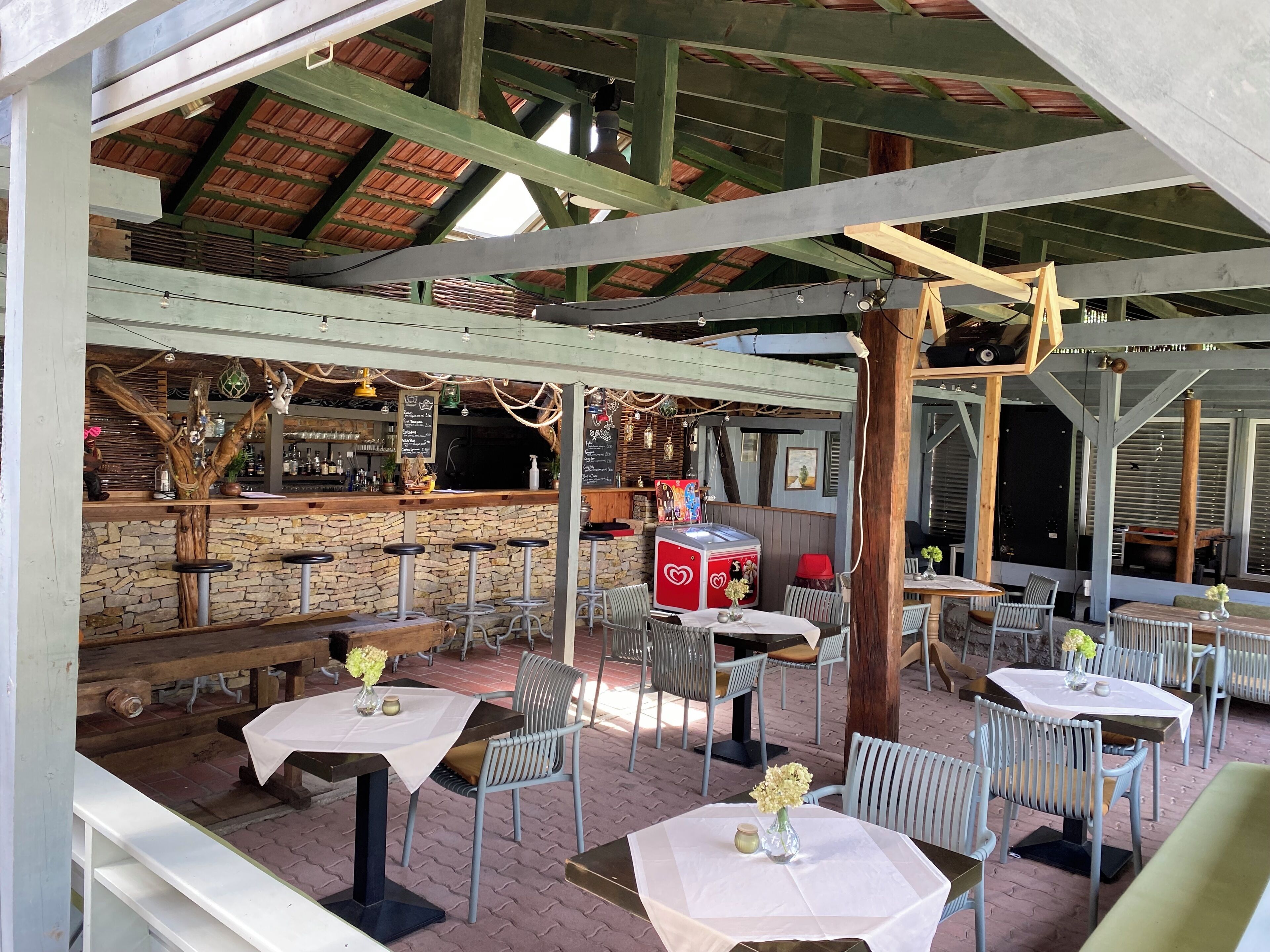 An outdoor patio area with stone walls, wooden beams, and metal chairs and tables.