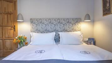 Een tweepersoonsbed met witte beddengoed en een hoofdbord met bloemen, twee bedlampjes en een vaas met bloemen.