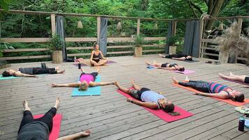 Un grupo de personas sobre esterillas de yoga en un entorno exterior con una terraza de madera y follaje de fondo.