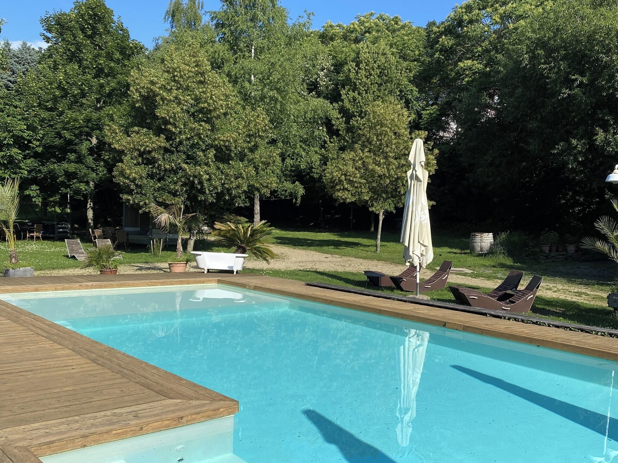 A swimming pool with a wooden deck, surrounded by trees and outdoor seating.