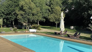 A swimming pool with a wooden deck, surrounded by trees and outdoor seating.