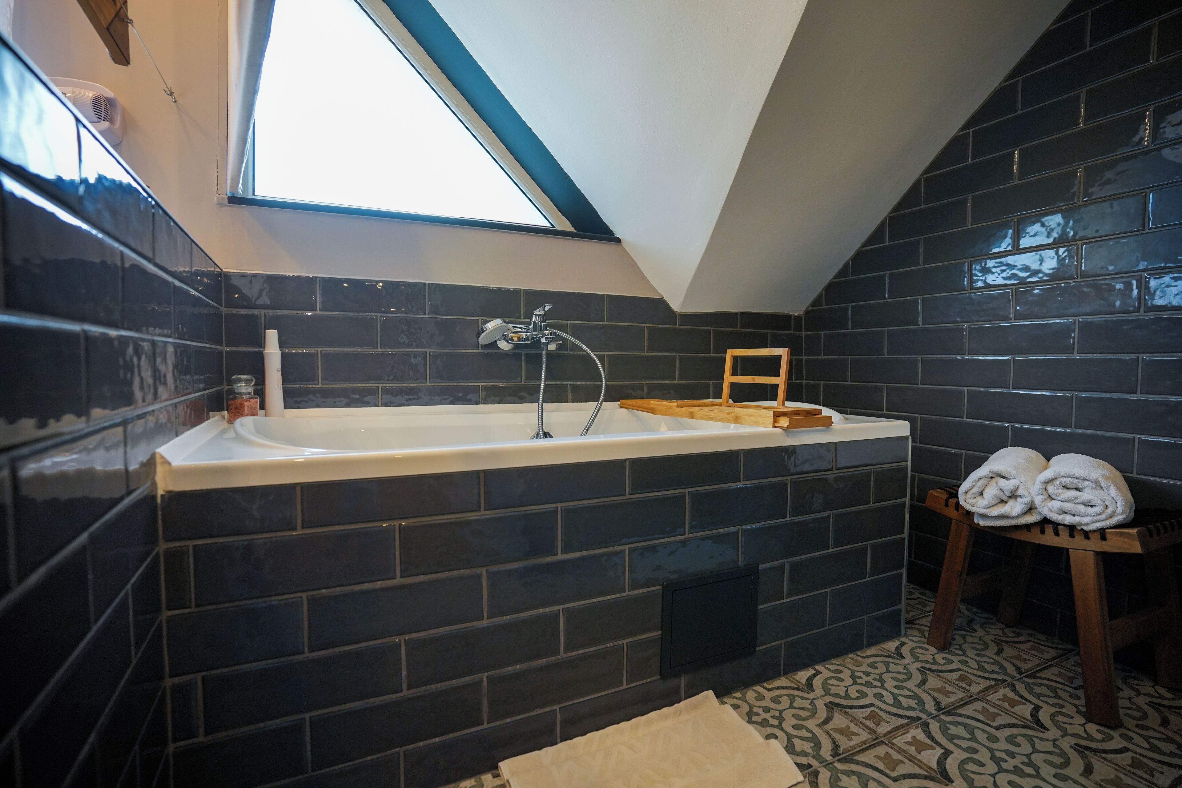A modern bathroom with a skylight, a freestanding bathtub, and a wooden stool with towels.