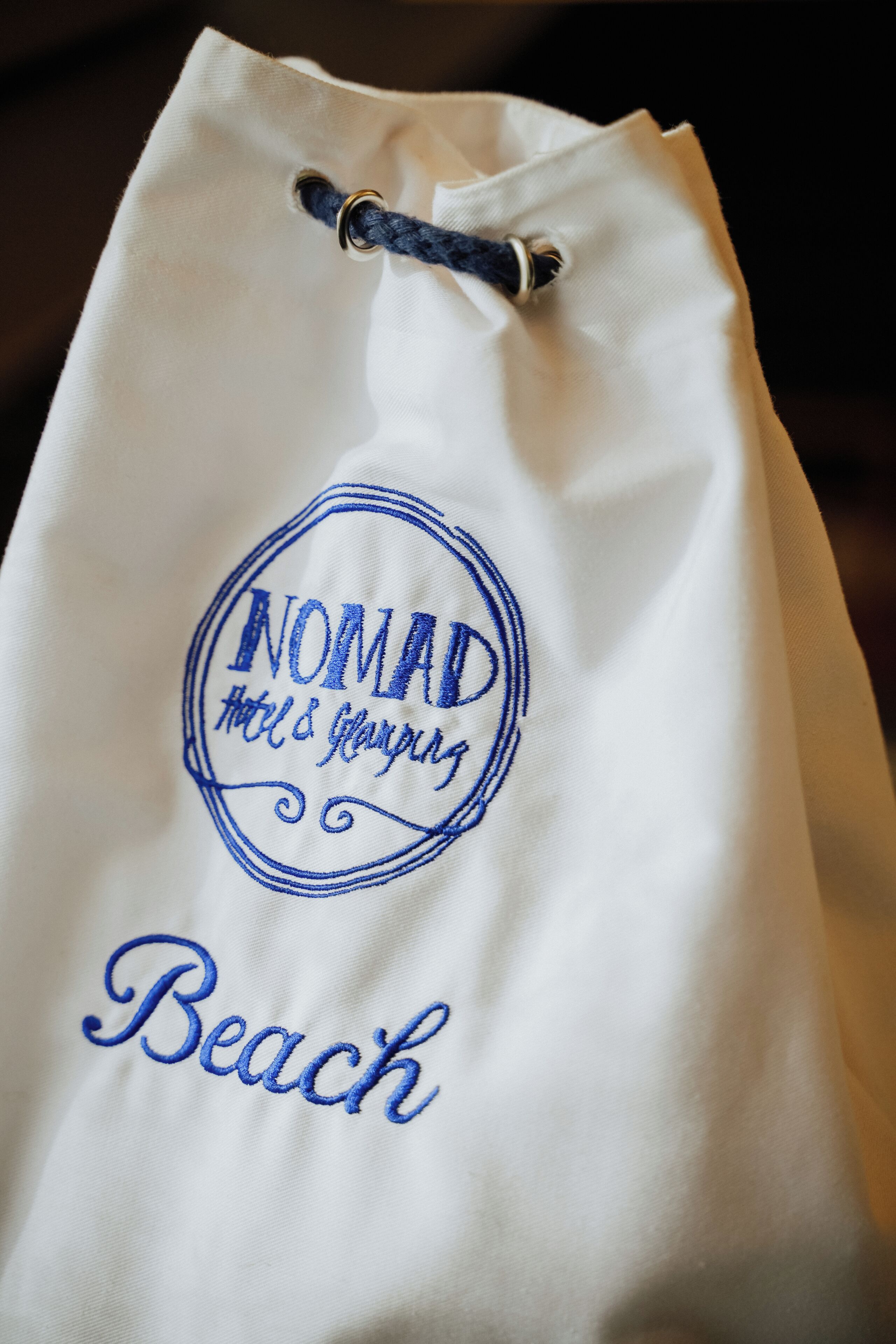 Eine weiße Tragetasche mit aufgesticktem Text, der „NOMAD Hotel & Spa“ und „Strand“ zeigt.
