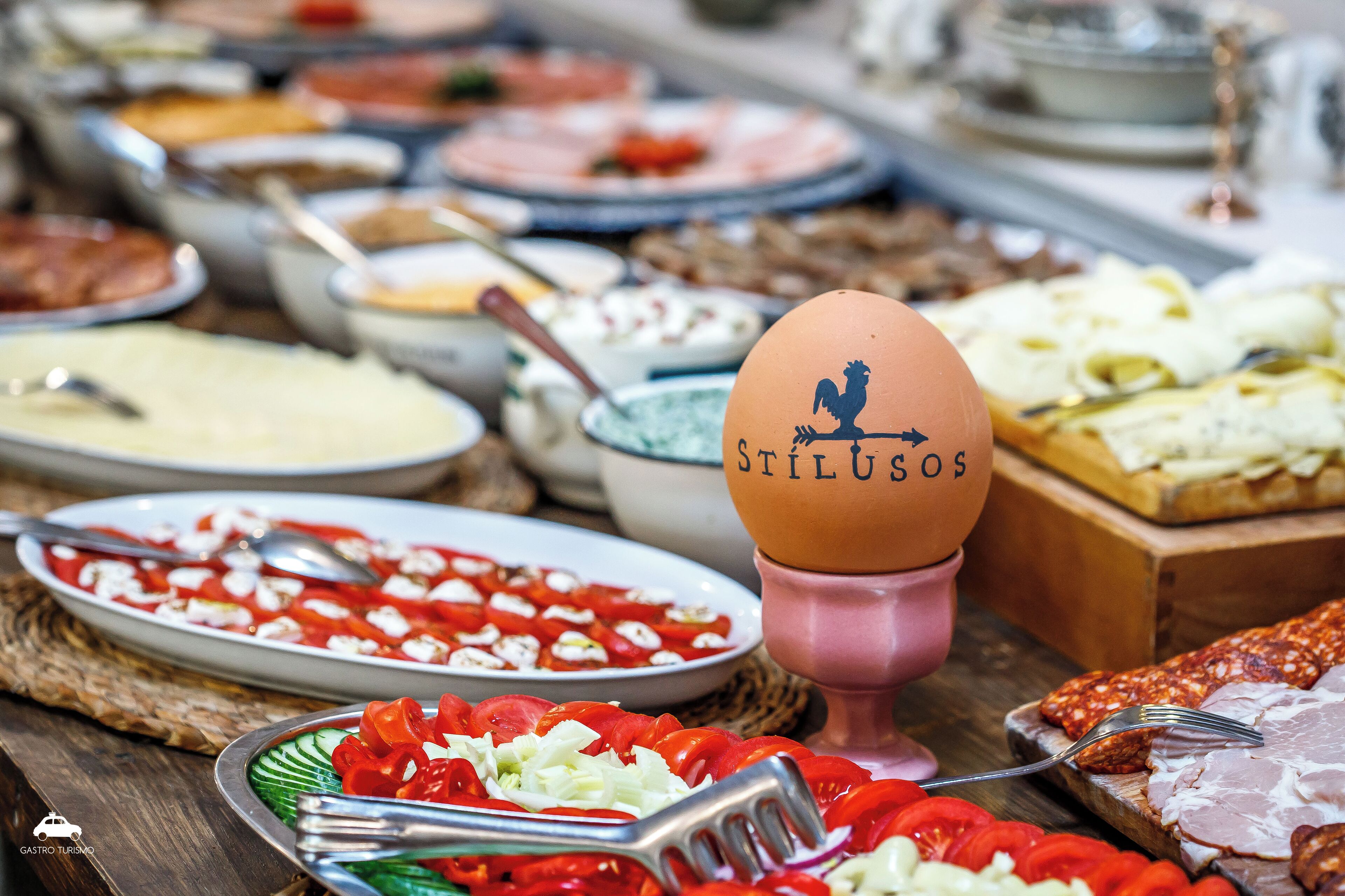 A variety of food items on a table, including a plate of tomatoes, a bowl of soup, and a slice of meat.