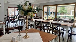 Un restaurante con varias mesas y sillas, un amplio ventanal que ofrece vistas al exterior, y un jarrón decorativo sobre una de las mesas.
