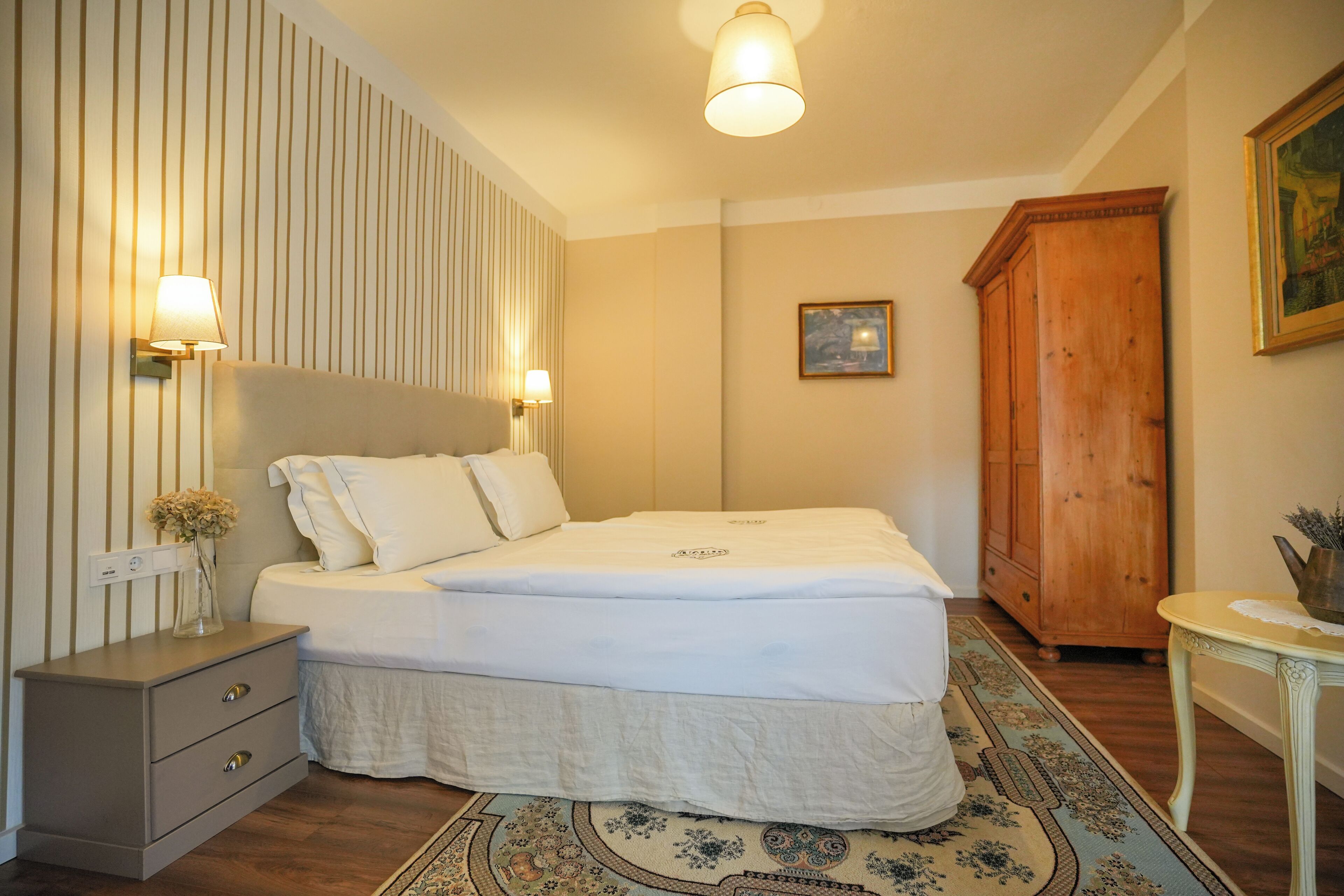 A neatly arranged bedroom with a bed, bedside tables, a wooden wardrobe, and a framed picture on the wall.