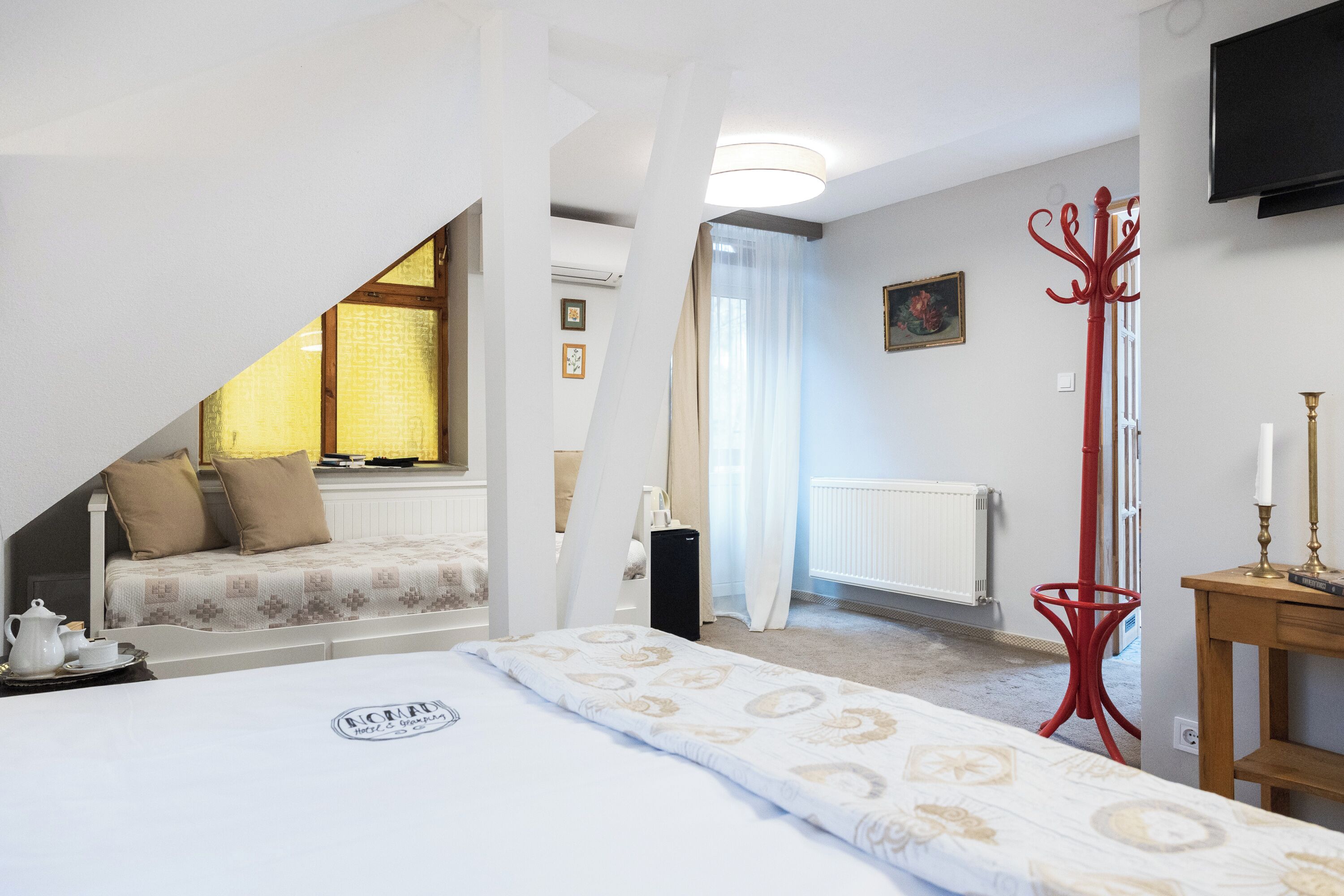 Une chambre à coucher avec un lit, une petite table avec une lampe, un radiateur et un téléviseur fixé au mur.