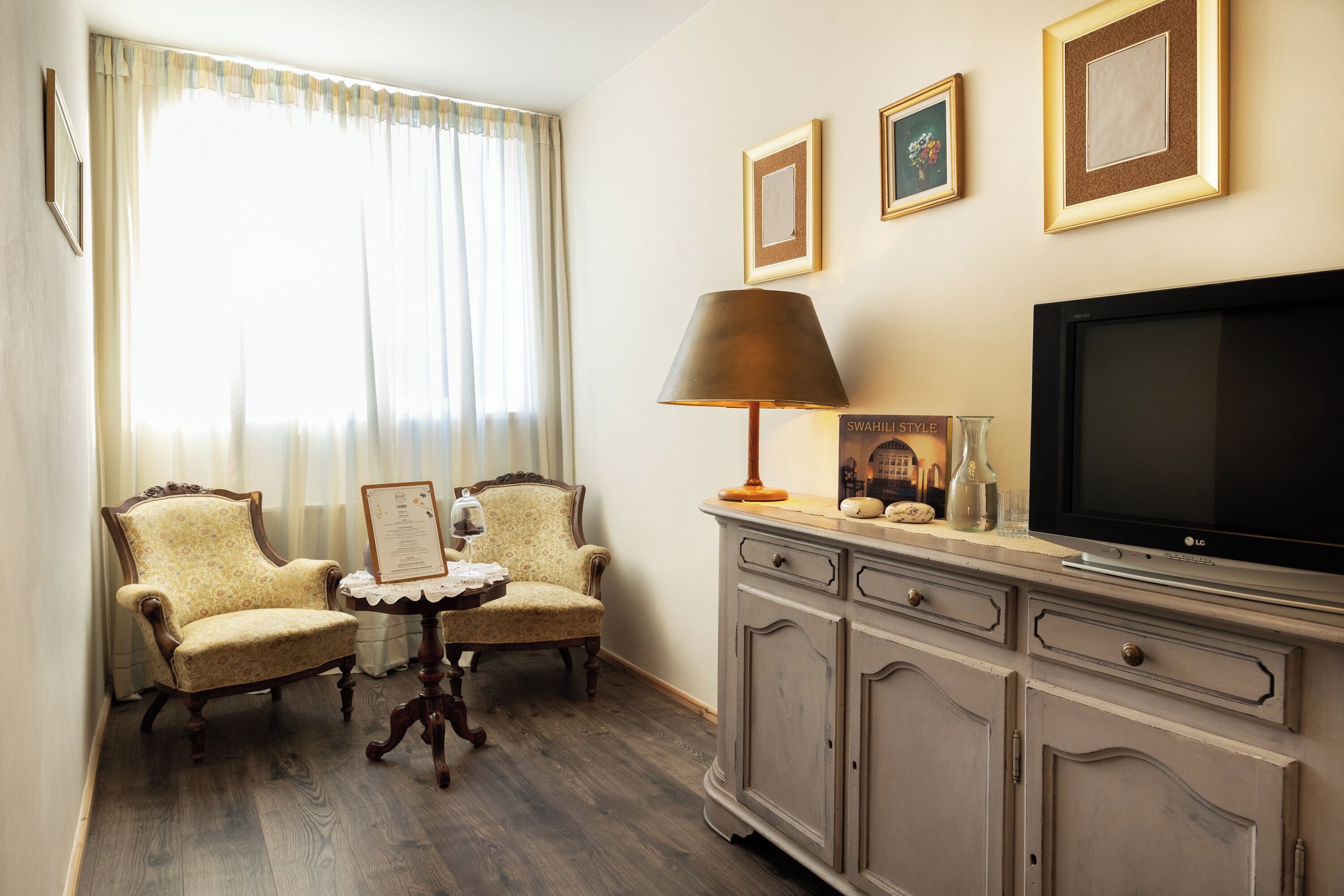 A room with two armchairs, a small table, a television, and a cabinet.