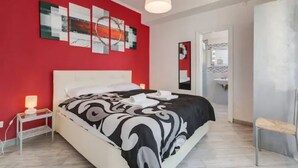 A modern bedroom with a red accent wall, a white bed, and a bedside table with a lamp. - Rome apartment penthouse with terrace spanish steps trevi fountain barberini (Roma)