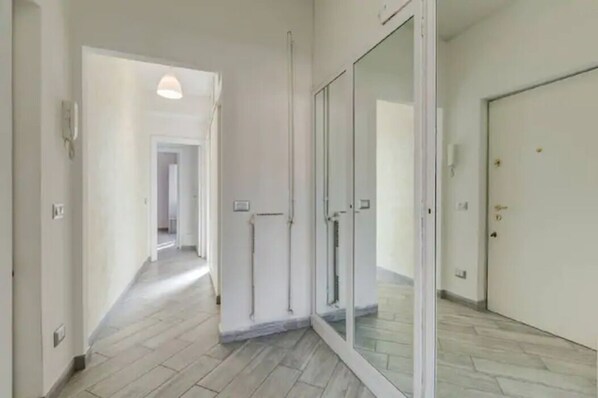 A hallway with a glass door leading to a room, a light fixture on the ceiling, and a tiled floor.