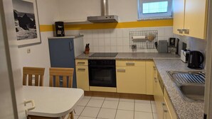 A compact kitchen with a stove, oven, and sink. There is a window above the sink and a small window on the wall.