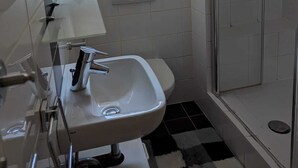 A bathroom with a glass shower enclosure, a sink with a mirror, and a window above the sink.