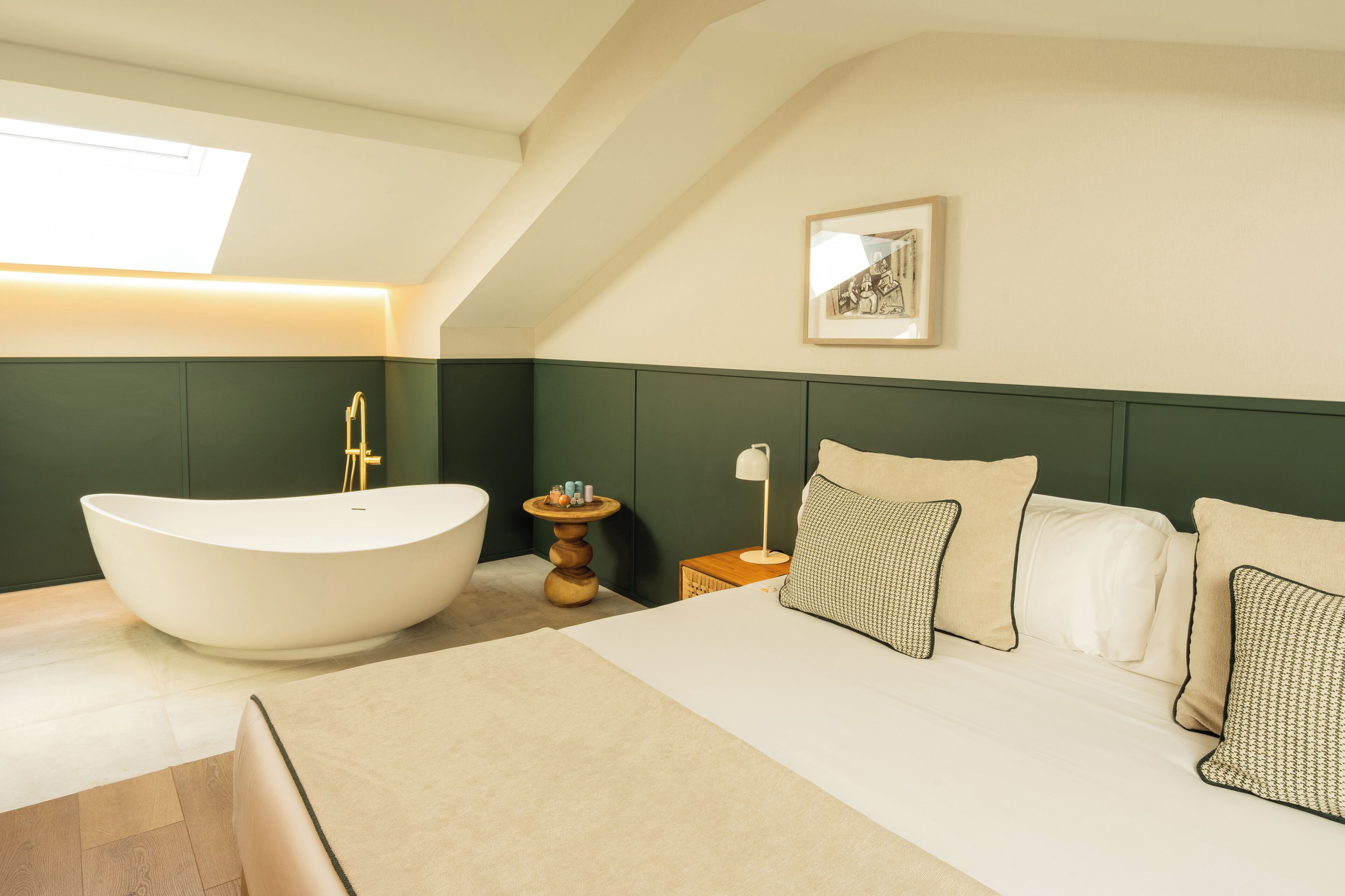 A modern bedroom with a large bathtub, a bed with multiple pillows, a small side table, and a framed picture on the wall.
