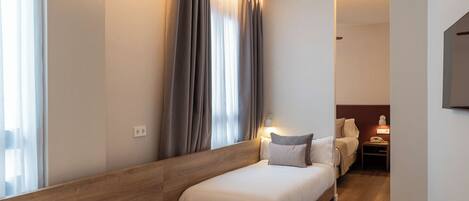 A hotel room with two single beds, a wooden headboard, a bedside table with a lamp, and a TV mounted on the wall.