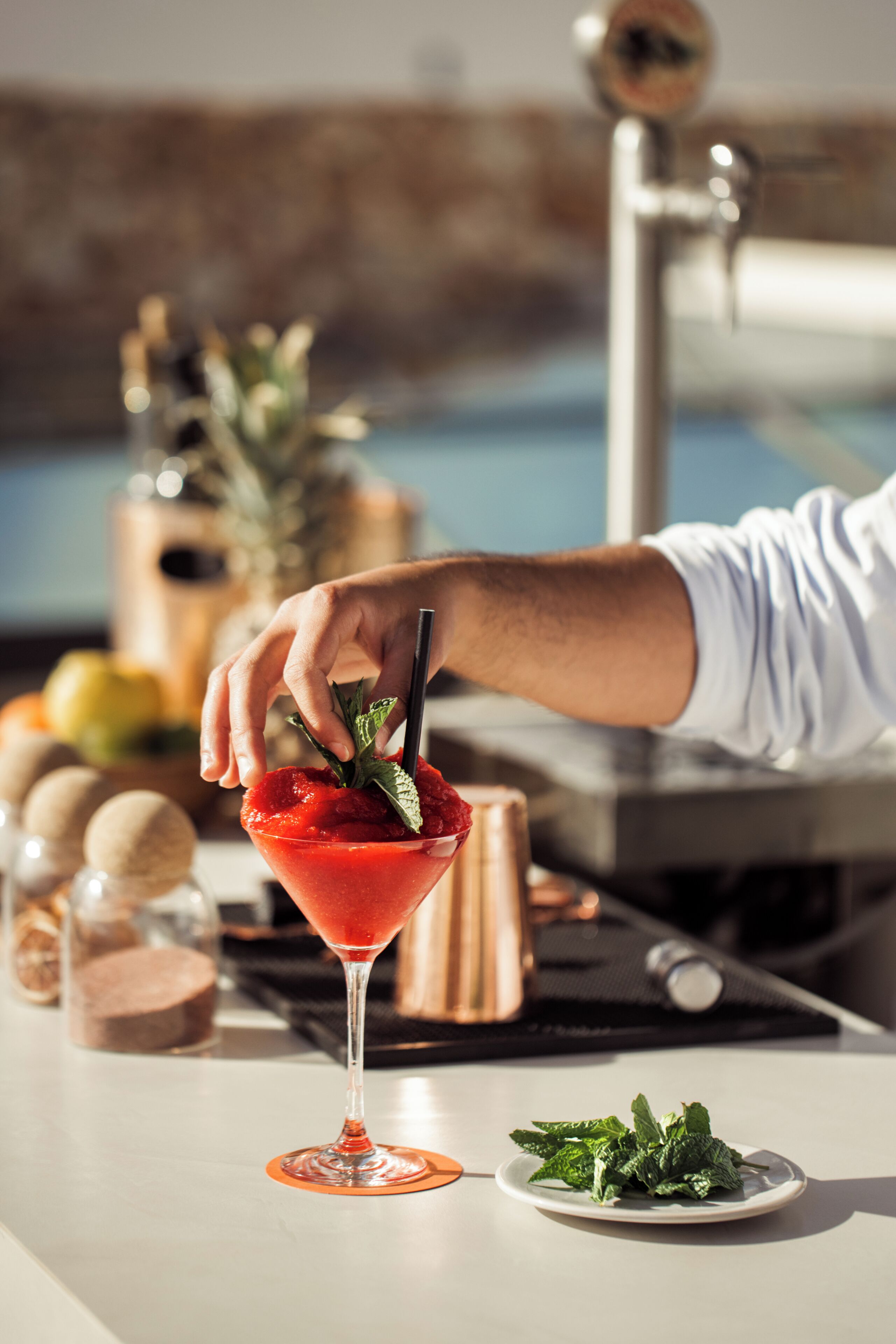 Un cocktail in un bicchiere da martini guarnito con foglie di menta, un piatto con foglie di menta e uno sfondo sfocato di un bar.