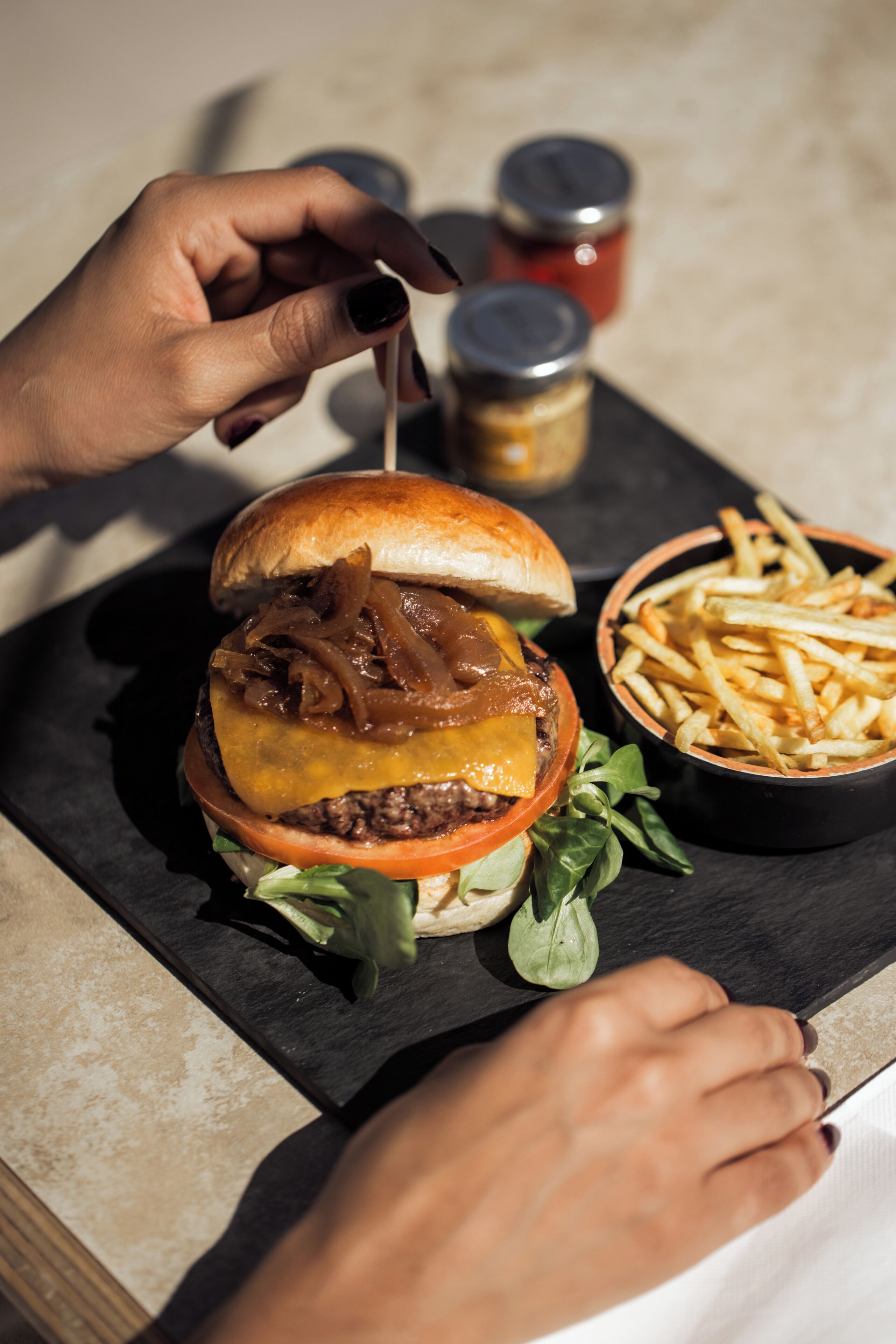 Un hamburger accompagné de frites, servi sur une assiette en ardoise noire.