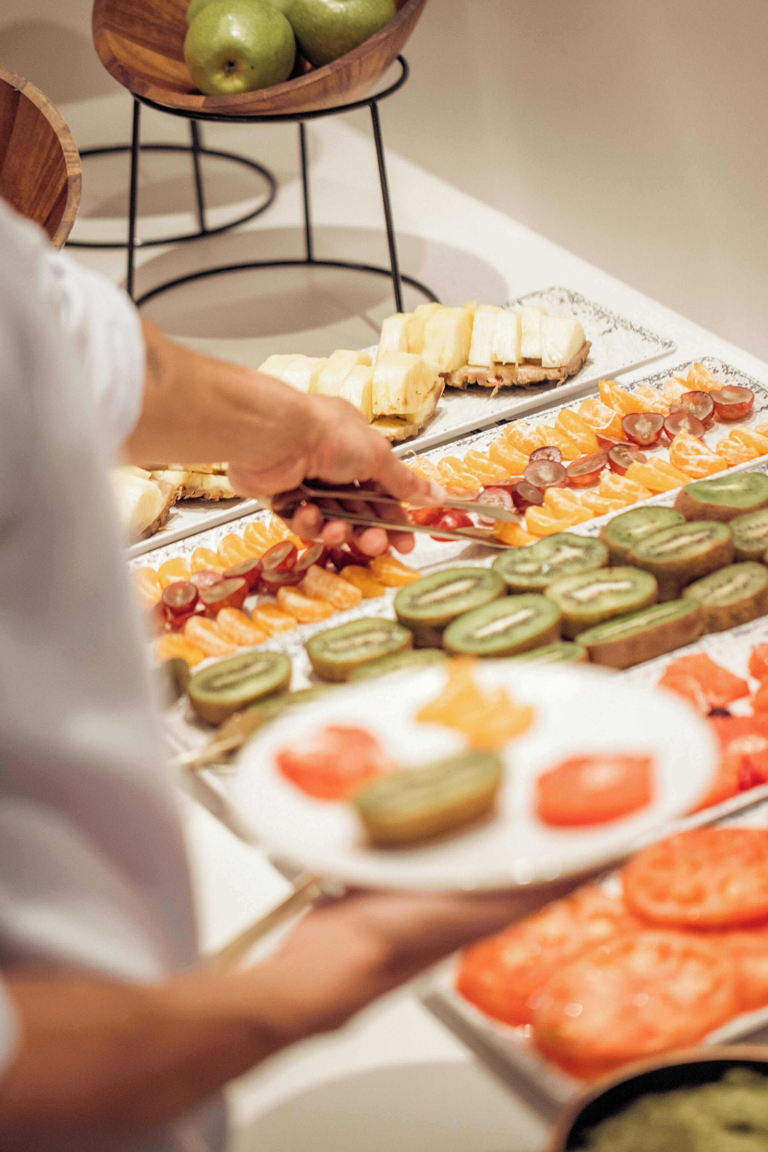 A buffet table with various fruits and a person serving food.