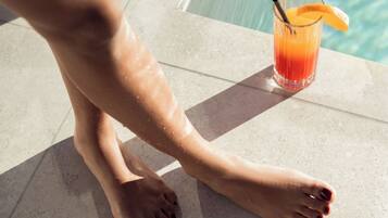 Zona junto a la piscina con un vaso de zumo de naranja y una rodaja de naranja al borde.