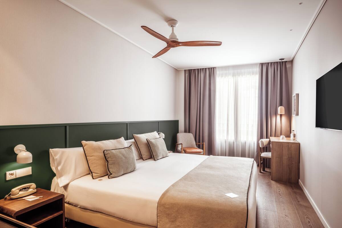 Une chambre d’hôtel équipée d’un lit, d’une table de chevet, d’une lampe, d’une chaise et d’un ventilateur de plafond.