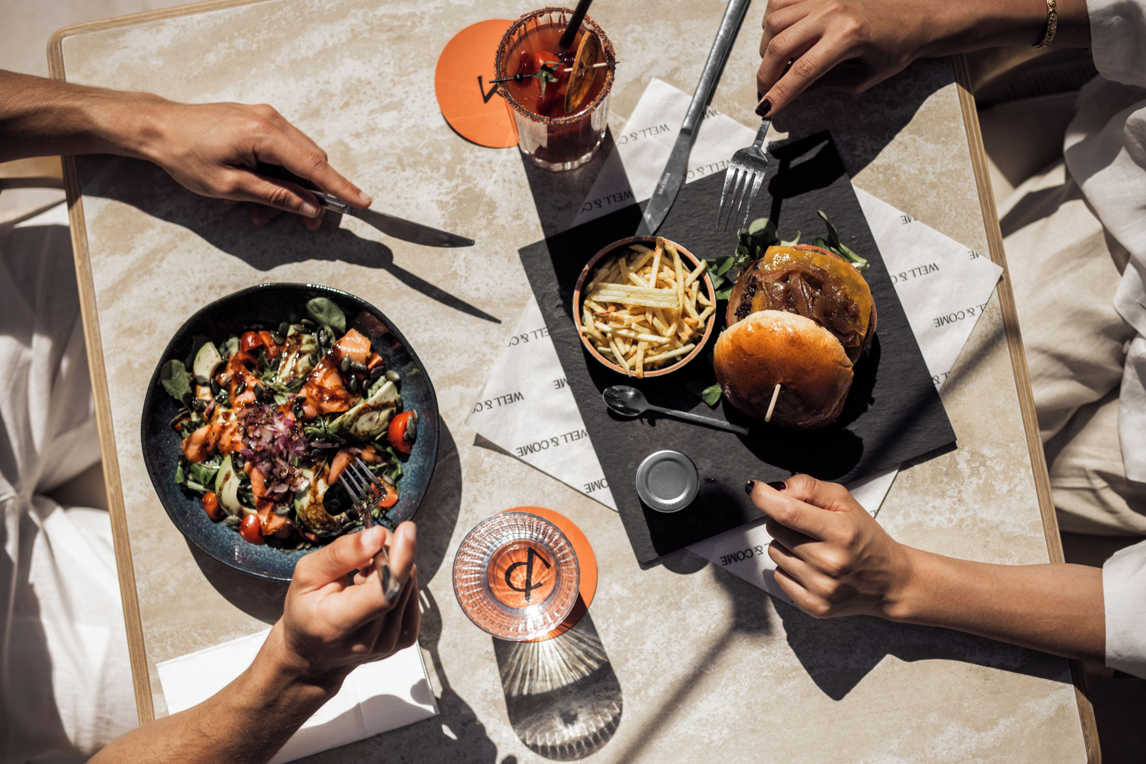 Una mesa de comedor con ensalada, hamburguesa, papas fritas y una bebida.