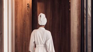 A person in a white robe walking down a hallway with wooden walls and a door marked with the number 21.