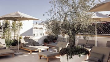 Una terraza en la azotea con sillones de descanso, sombrillas y plantas en macetas.
