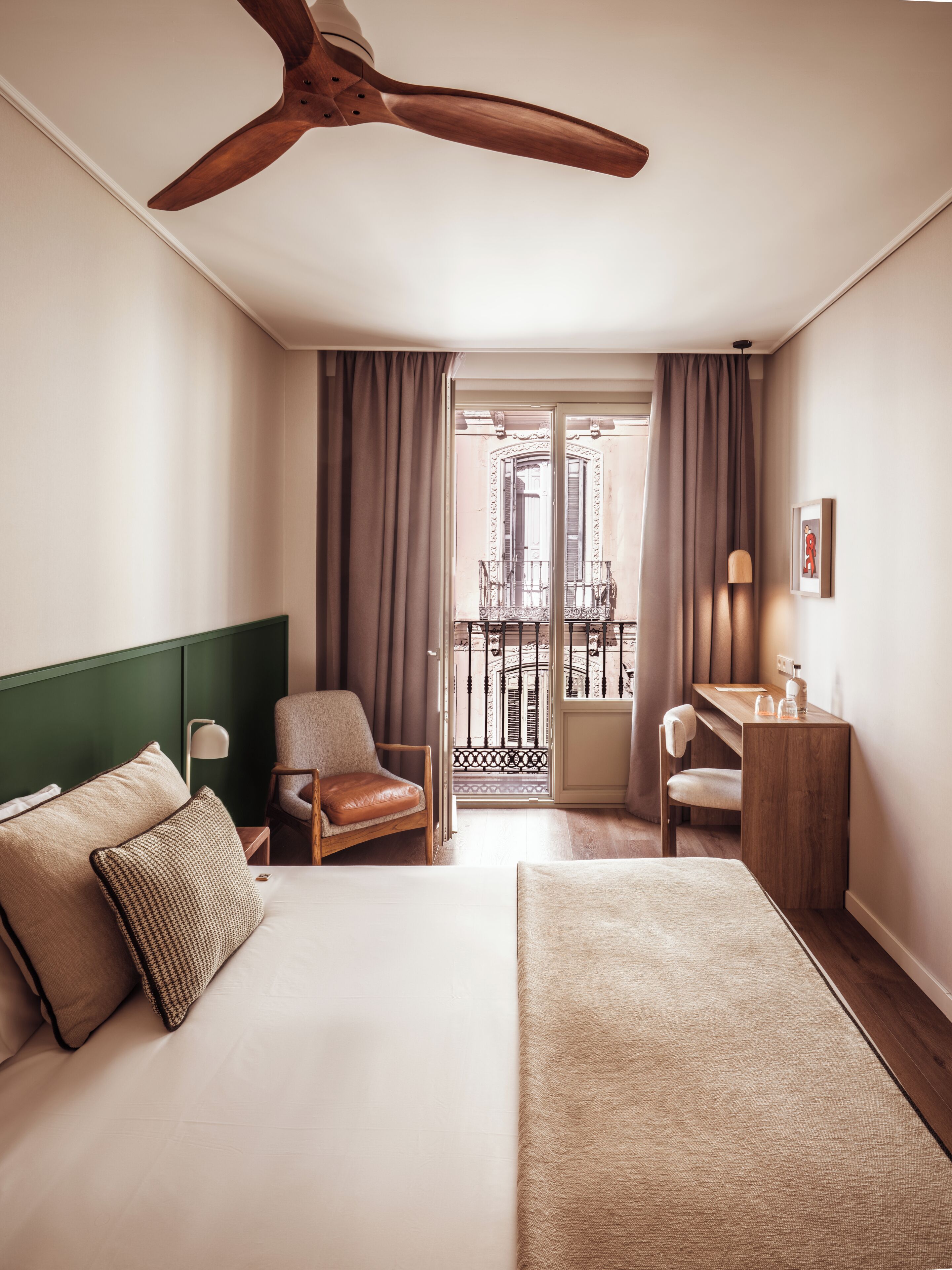 A hotel room with a bed, a desk, a chair, a balcony with a view, and a ceiling fan.