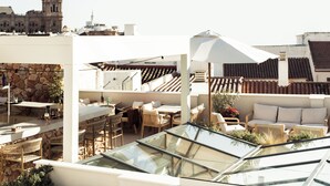 A rooftop terrace with outdoor seating, a stone wall, and a view of historic buildings. - Hotel Well and Come Malaga (Málaga)