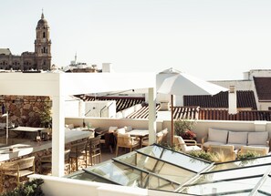 A rooftop terrace with outdoor seating, a stone wall, and a view of historic buildings. - Hotel Well and Come Malaga (Málaga)