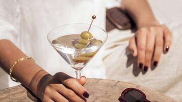 Una copa de martini con aceitunas, unas gafas de sol y un bol de patatas fritas sobre una mesa de madera.