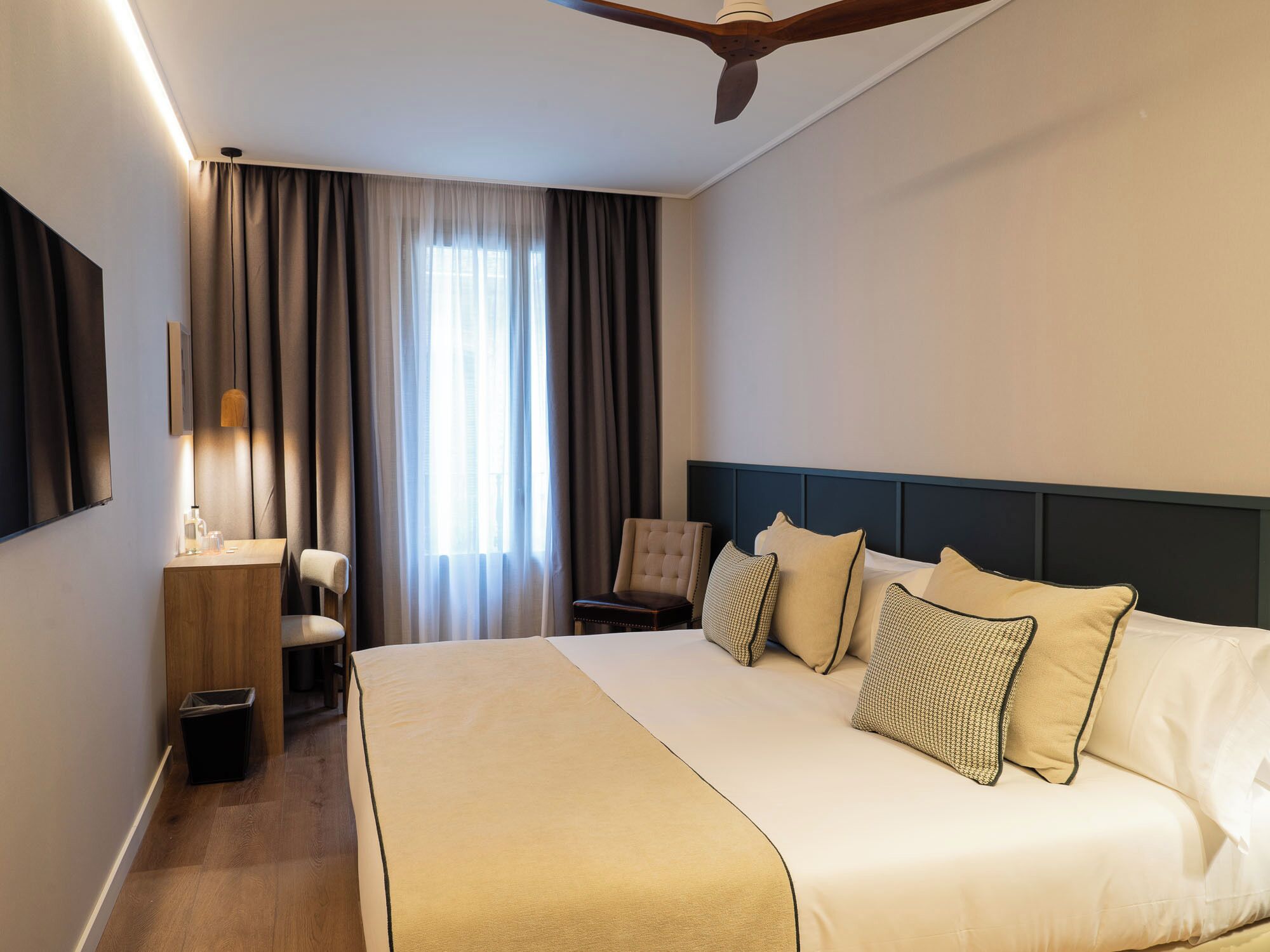 A hotel room with a large bed, a chair, a desk with a lamp, and a window with curtains.