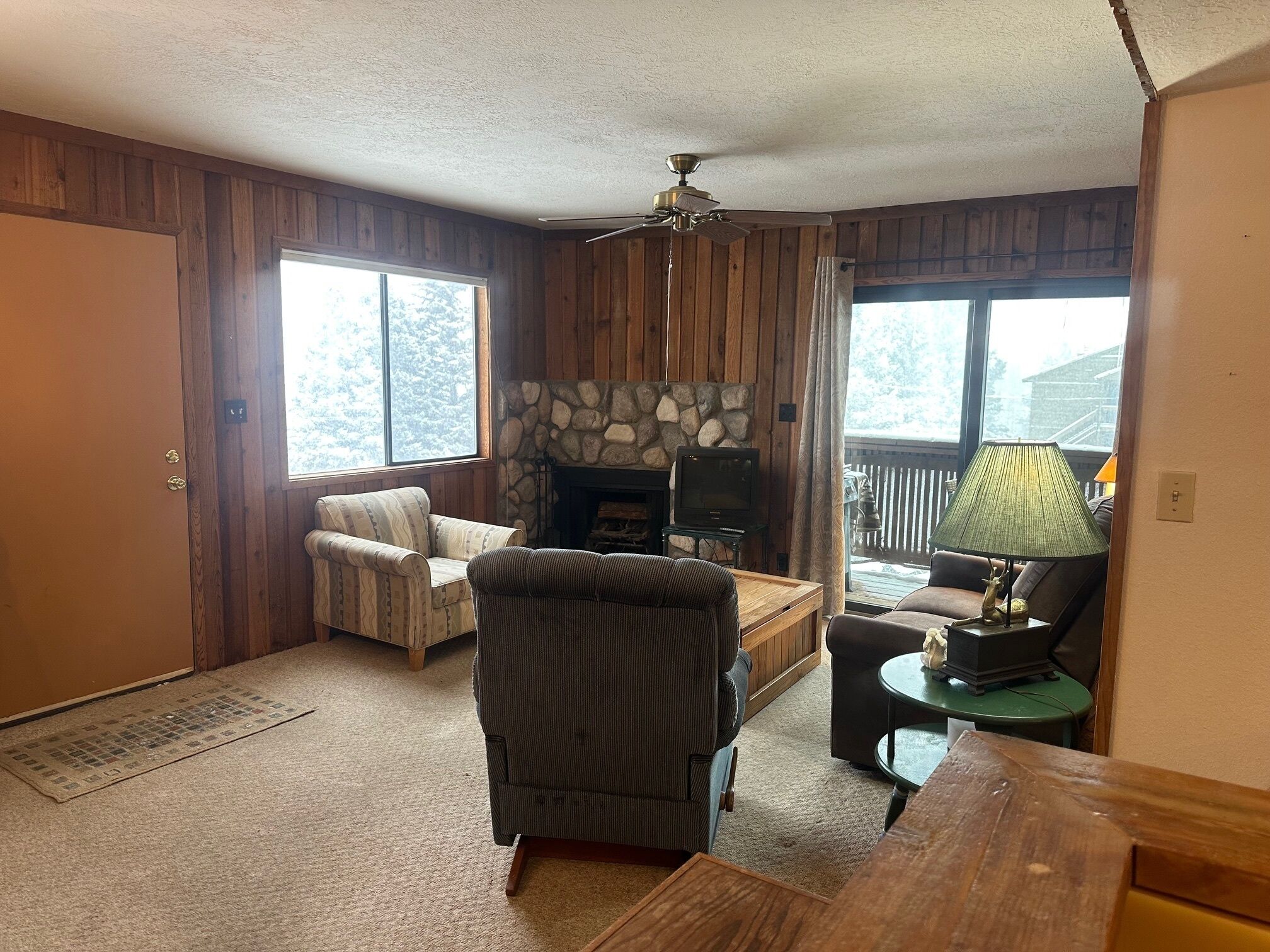 A cozy living room with a stone fireplace, a television, and a wooden ceiling fan.
