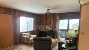 Un salon chaleureux avec une cheminée en pierre, un téléviseur et un ventilateur de plafond en bois.