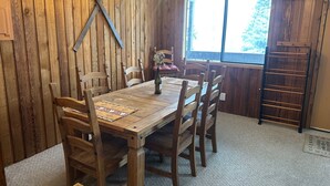 Une salle à manger en bois, avec une table et des chaises, un lustre et une fenêtre donnant sur les arbres.