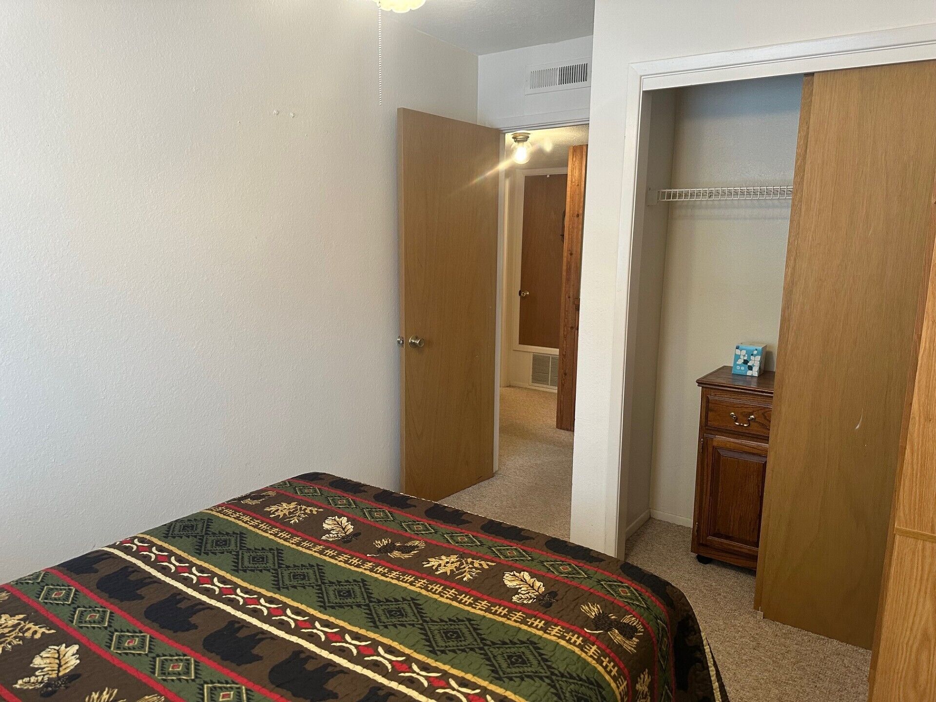 Une chambre à coucher avec un lit, une armoire en bois et une porte donnant sur une autre pièce.
