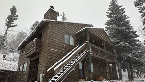 Une cabane en bois avec un escalier menant à l’entrée, entourée d’arbres couverts de neige.