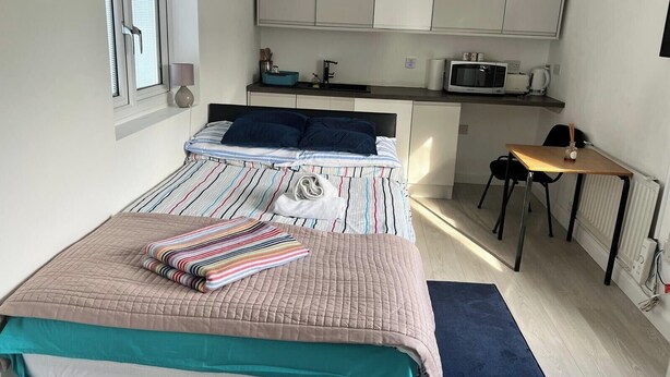Ein kleines Schlafzimmer mit Bett, Schreibtisch und Küchenzeile.