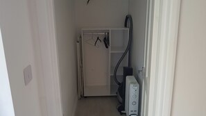 Een smalle gang met een witte deur, een radiator en een stofzuiger.